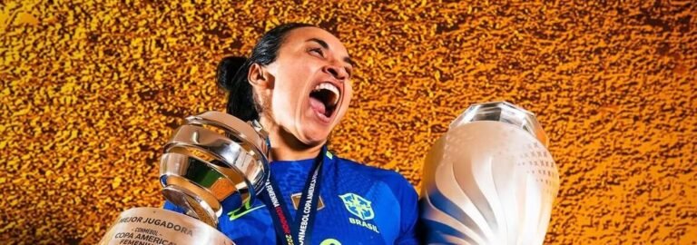 Jogadora da Seleção Brasileira feminina, de camisa azul nº 10, comemora gritando enquanto ergue dois troféus — o da Copa América Feminina e o de melhor jogadora — usando medalha dourada, diante de fundo laranja texturizado