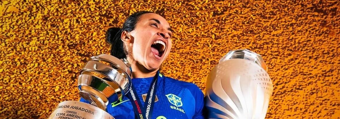 Jogadora da Seleção Brasileira feminina, de camisa azul nº 10, comemora gritando enquanto ergue dois troféus — o da Copa América Feminina e o de melhor jogadora — usando medalha dourada, diante de fundo laranja texturizado